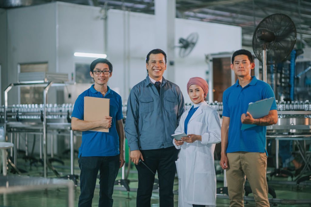 Asian manager and multiracial group of factory bottling plant workers looking at camera smiling